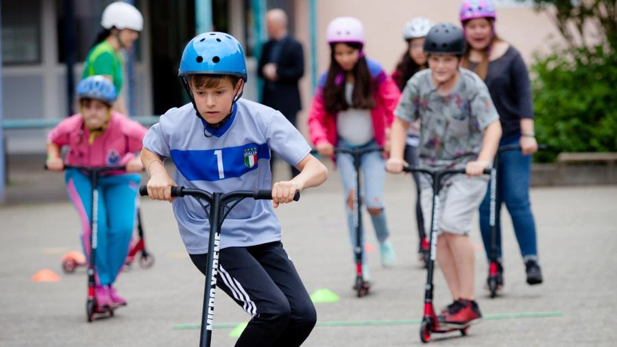 Bild zeigt Kinder mit Helm beim Fahren von Tretrollern.