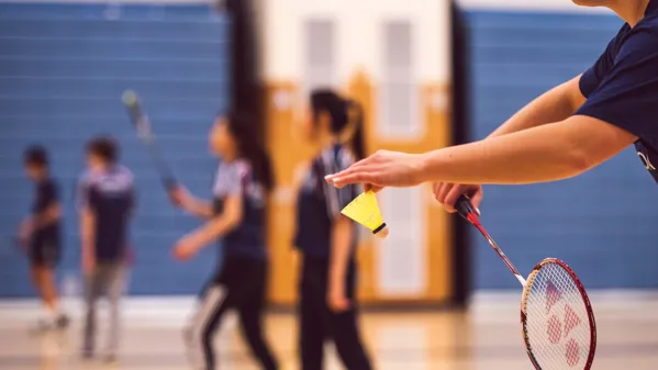 Bild zeigt Kinder beim Badmintonspiel. Zoom auf den Schläger beim Aufschlag.