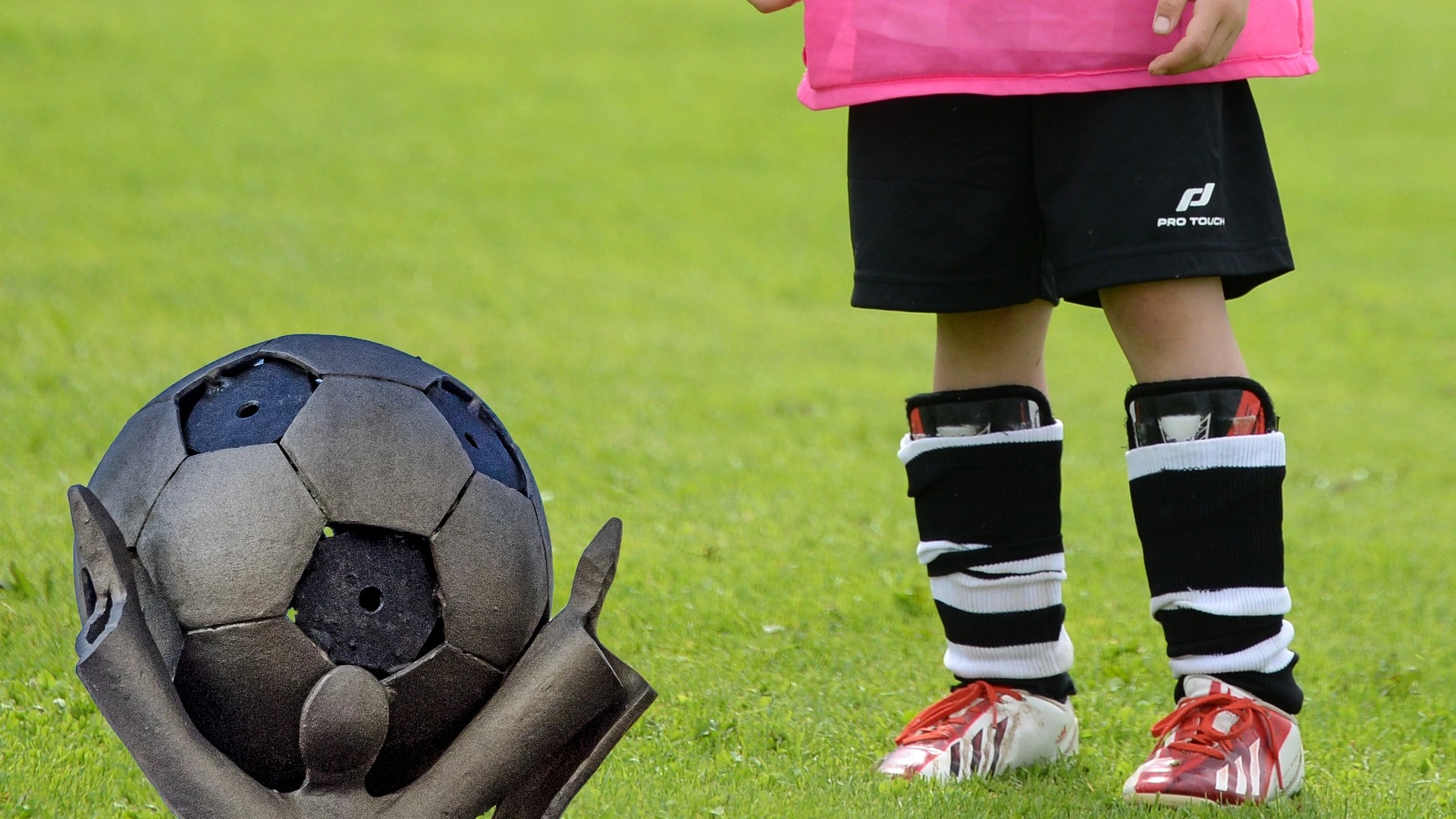 Bild zeigt noch die Beine eines Kindes mit Fußballausrüstung hinter einem Fußballpokal
