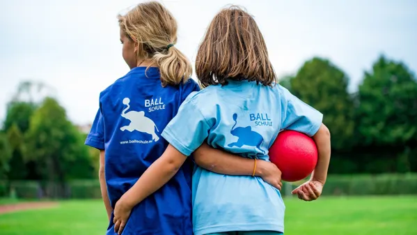 Bild zeigt zwei Kinder mit den Armen um die Schulter des anderen und einem Ball