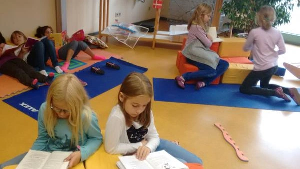 Bild zeigt mehrere Schülerinnen, die im Raum verteilt in Zweiergruppen zusammen sitzen und an Texten arbeiten.