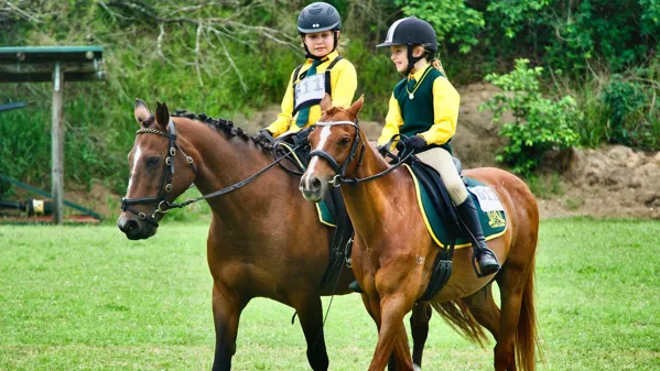 Bild zeigt zwei Jugendliche beim Reiten auf dem Pferd mit Helm.
