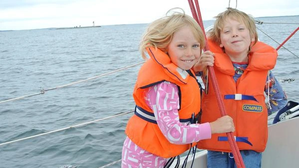 Bild zeigt zwei Kinder auf einem Segelboot mit Rettungswesten.