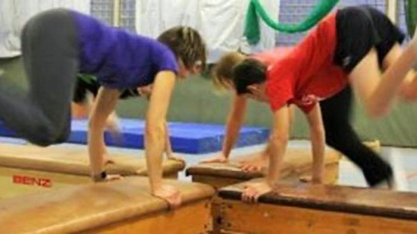 Bild zeigt Kinder, die sich mit den Armen an großen Kästen festhalten und von Tuch zu Tuch über den Kasten springen.
